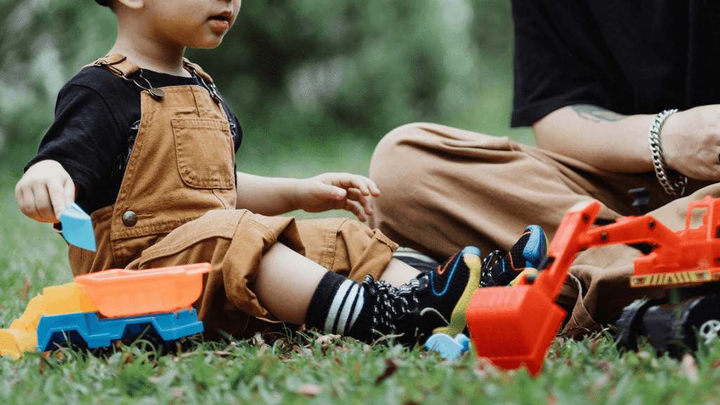 Caregiver and child playing together outdoors in the grass.