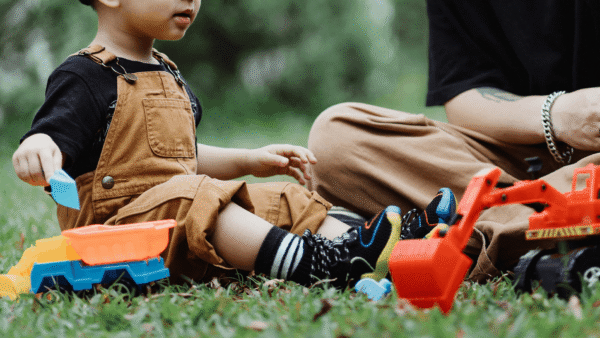 Caregiver and child playing together outdoors in the grass.