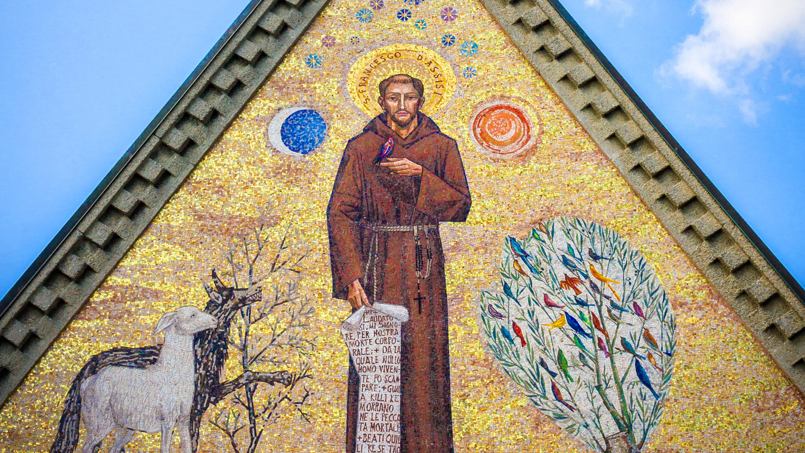 A warm, vibrant mosaic of St. Francis holding a scroll in one hand and a bird in the other. He stands between a bush full of birds on one side and a sheep and wolf on the other. The moon is near his head on his right and the sun is near his head on his left. 