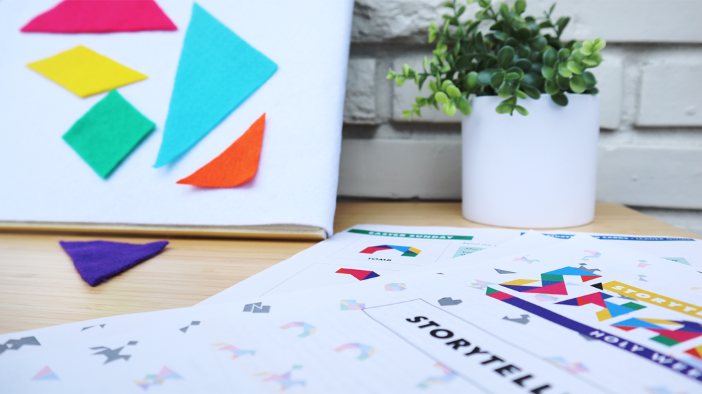 A close up of Storytelling with Shapes adapted for use on a felt board. Colorful tangram shapes hang on the board and one lays on the table. In the background there is a plant in a white pot and a white brick wall.