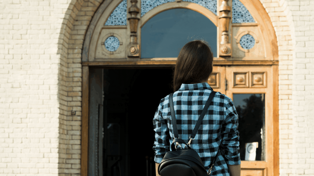 A teenager wearing a backpack stands outside a traditional church doorway, symbolizing the experience of queer youth navigating moderate church spaces.