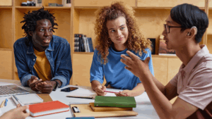 A group of diverse young people sits around a table discussing ideas, highlighting co-leadership, creativity, and participatory youth ministry planning.
