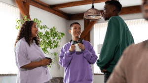Three young adults engage in relaxed conversation while holding mugs, showcasing authentic relationships and informal connection in faith-based community spaces.