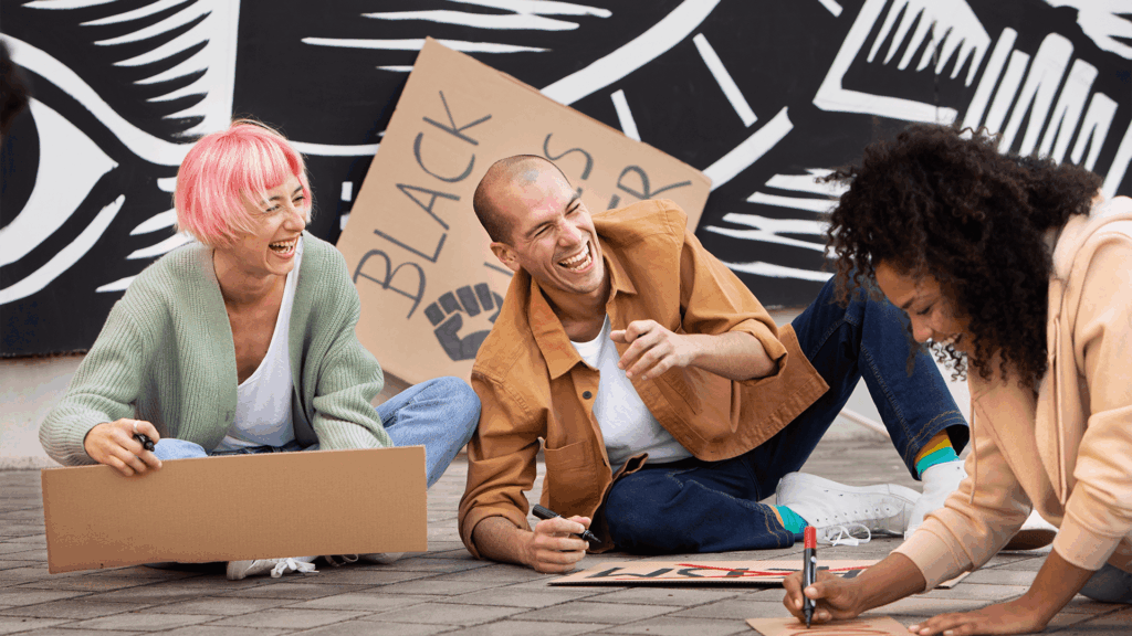 Group of young adults laughing together while making protest signs, including one that reads “Black Lives Matter”