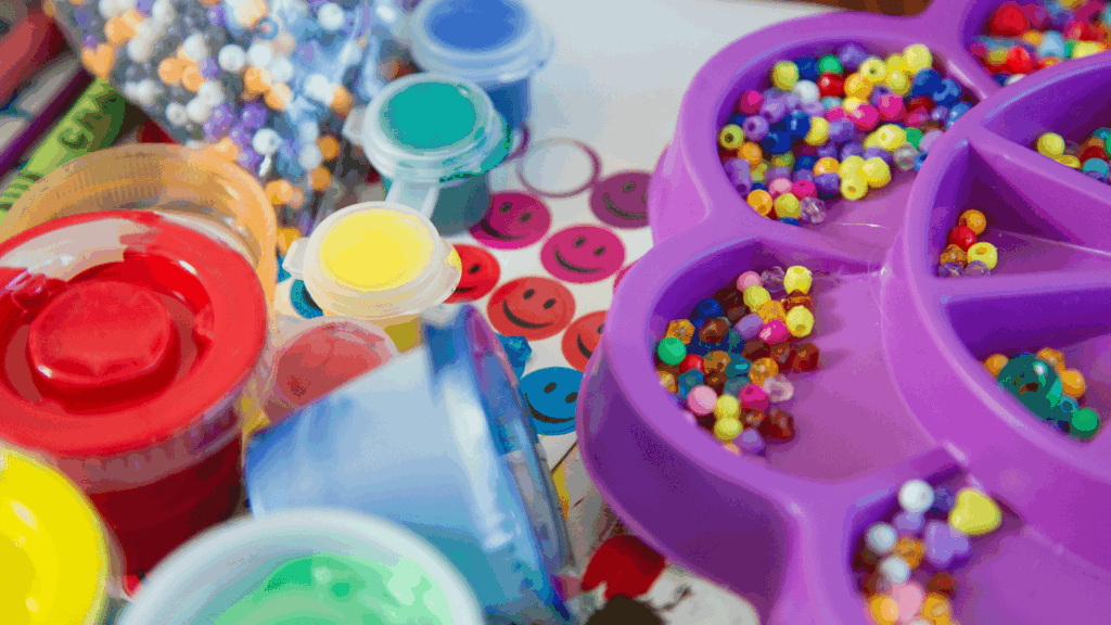 Assorted plastic craft supplies including beads, stickers, and paints, highlighting materials to swap for sustainable alternatives.