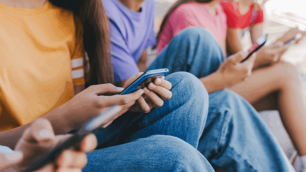 Close-up of several teenagers sitting together outdoors, each holding a smartphone, representing how young people spend time online and on social media platforms like TikTok.