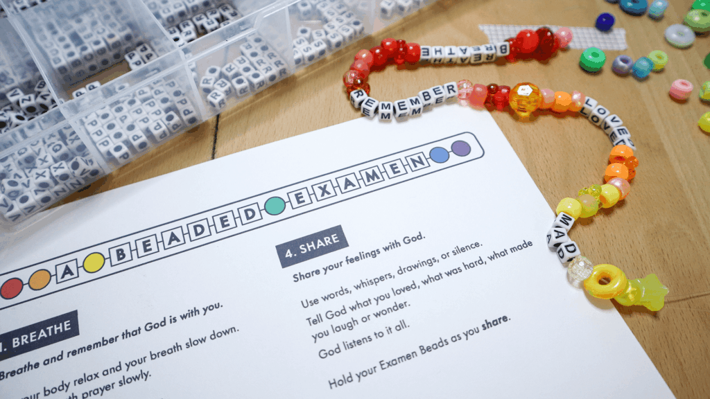 A completed Beaded Examen prayer strand with letter beads spelling Breathe, Remember, and Loved beside a printable guide and a box of alphabet beads.