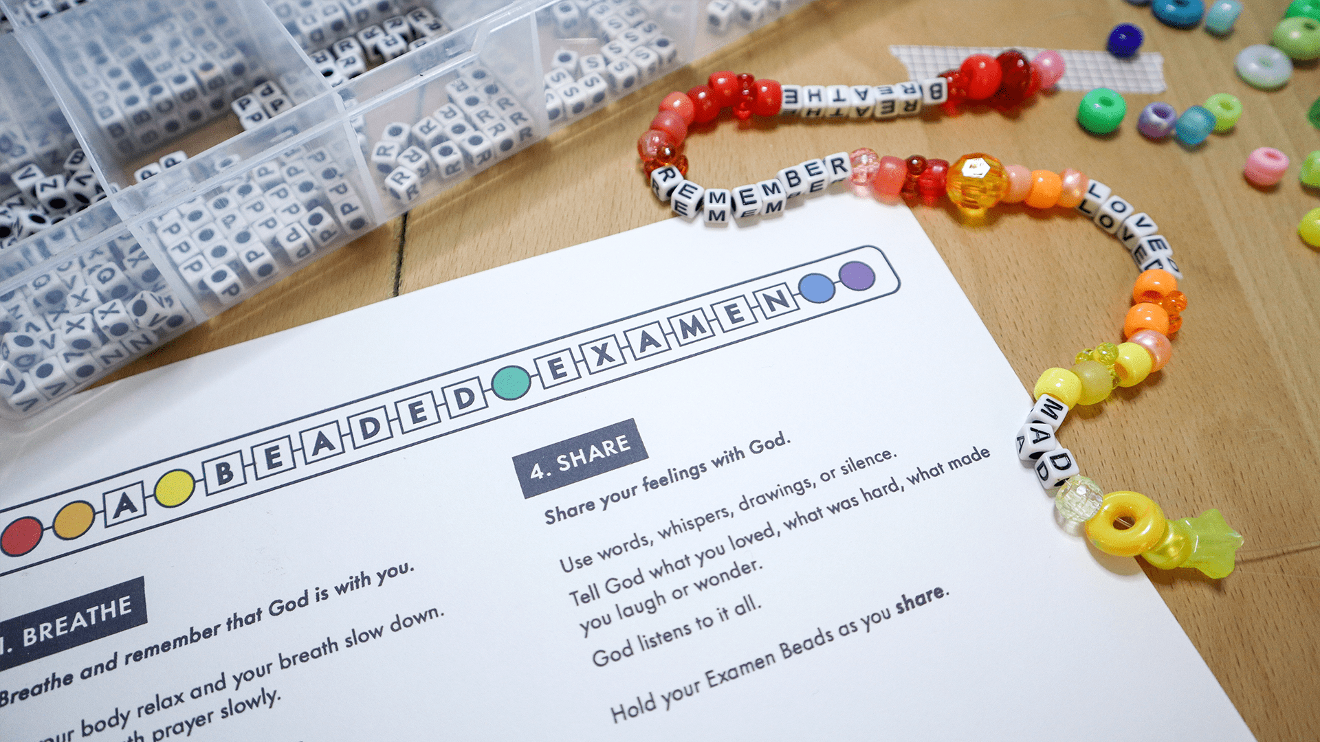A completed Beaded Examen prayer strand with letter beads spelling Breathe, Remember, and Loved beside a printable guide and a box of alphabet beads.