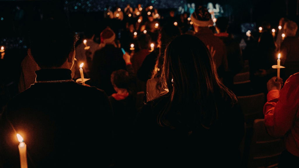 A congregation holding lit candles during a dark, candlelight Christmas service, viewed from behind several worshipers.