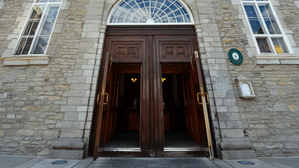 Large wooden double doors of a stone church propped open, revealing warm interior light inside.