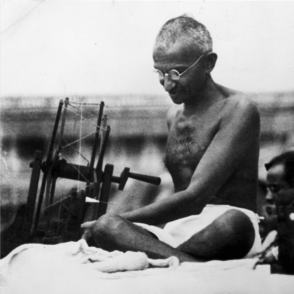 Mahatma Gandhi seated and spinning thread on a traditional spinning wheel as part of the khadi movement.