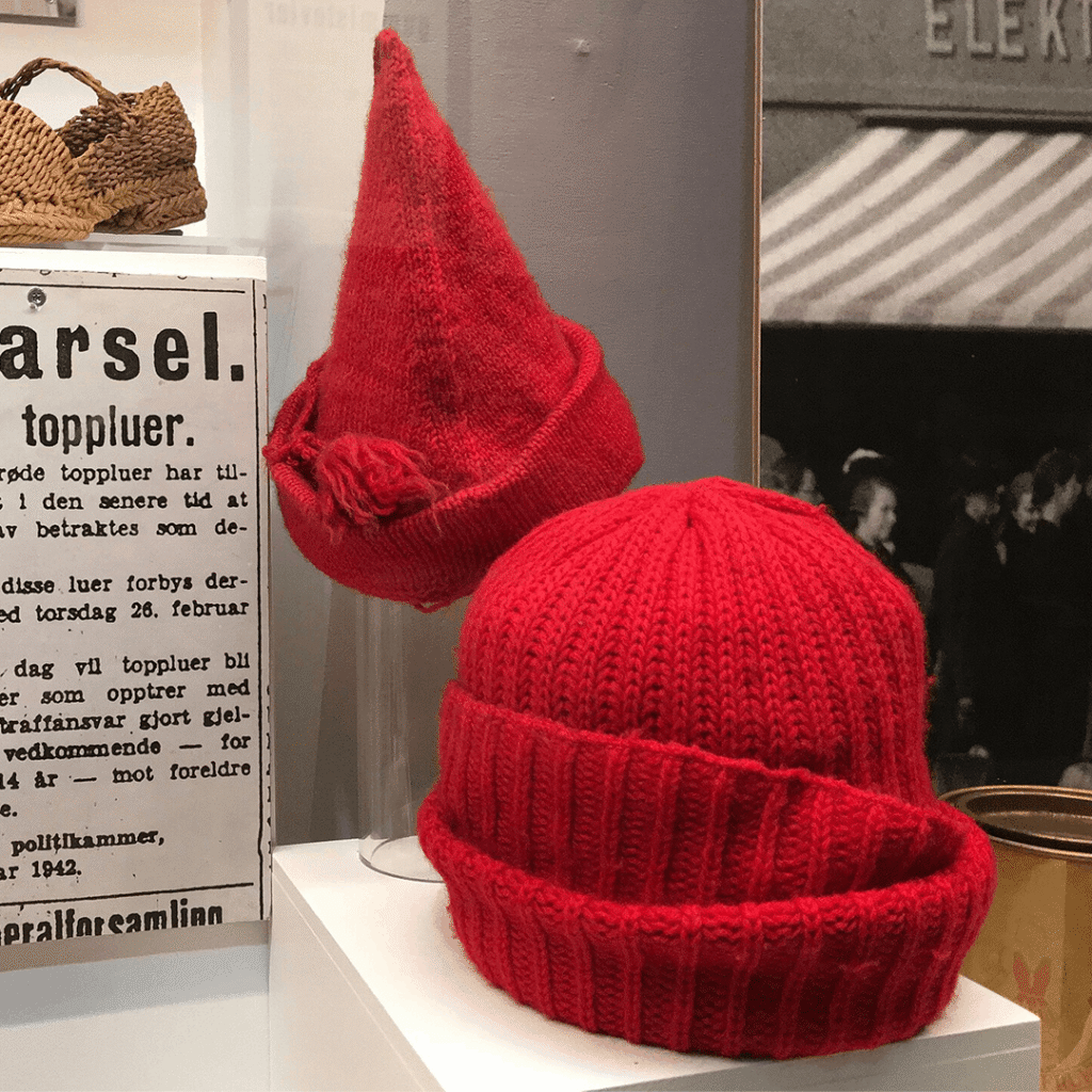 Two red knitted caps displayed in Norway’s WWII Resistance Museum beside a notice banning the hats as symbols of resistance in 1942.