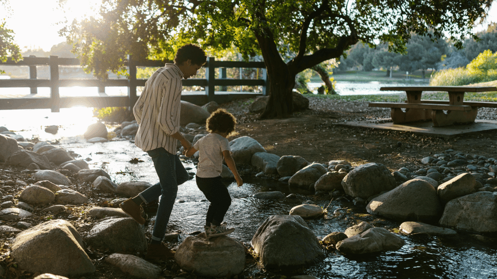 Parent and child holding hands while walking across rocks in a stream, showing trust and guidance