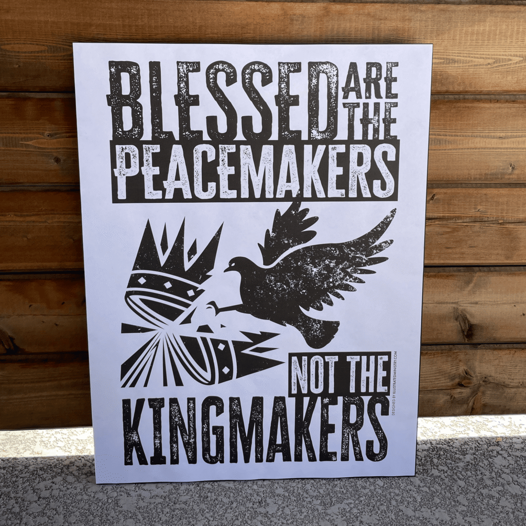 Protest sign "Blessed are the Peacemakers Not the Kingmakers" against wood background.