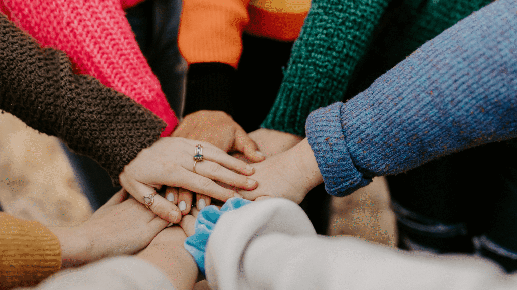 A group of volunteers place their hands together in a circle, symbolizing teamwork, trust, and commitment.