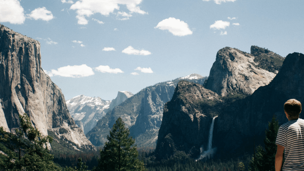 A teen enjoying a view of mountains, cliffs, and waterfalls.