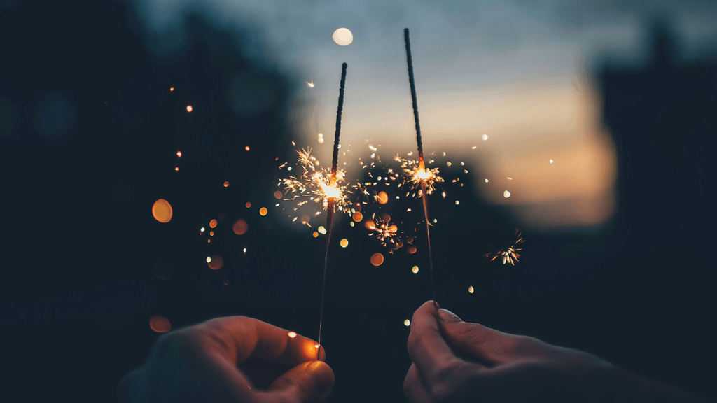 Two people hold glowing sparklers against a dark evening sky.